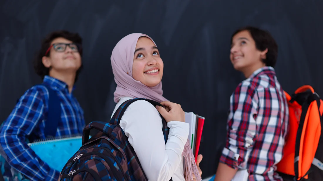 Three students with books and backpacks looking ahead